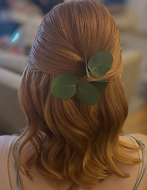 Half-up bridesmaid hairstyle with soft waves and a green leaf hair accessory on short hair.