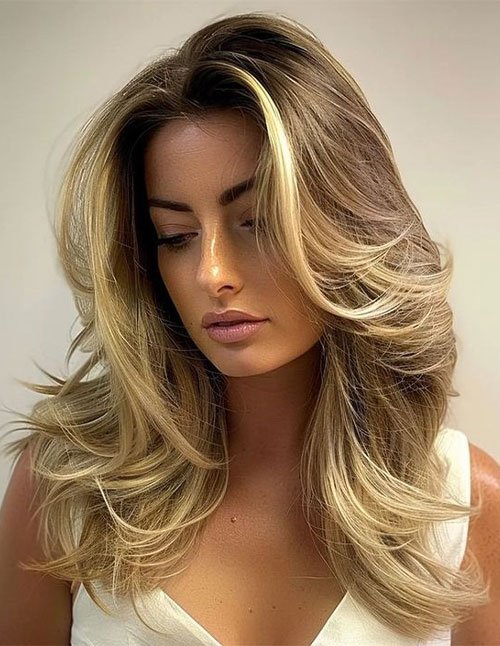 One woman with medium-length layered blonde hair styled with lots of volume and a soft blowout, looking downward.