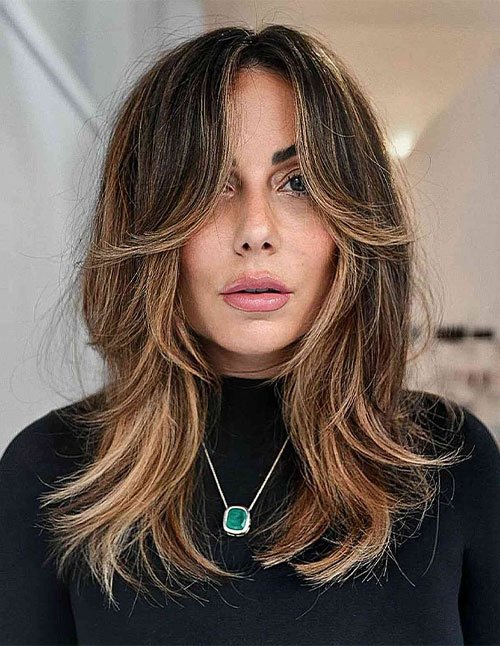 One woman with medium-length layered hair styled with a middle part and soft, feathered ends, photographed indoors.