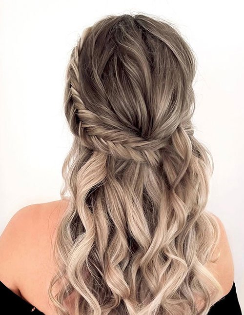 Back view of a woman with ash-blonde hair styled in half-up boho braids, featuring loose textured braids blended into soft, flowing waves.