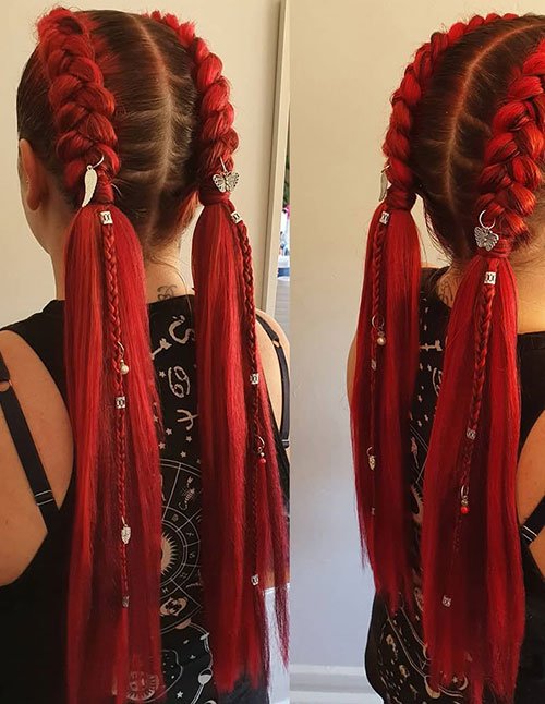 Back view of a woman with bright red hair styled in half-up boxer braids, featuring two tight Dutch braids secured into long ponytail sections with decorative hair cuffs.