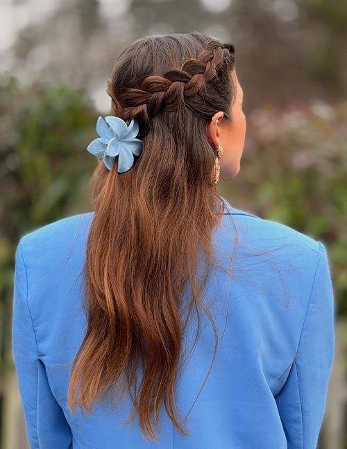 Back view of a woman with long brown hair styled in a half-up crown braid, secured with a light blue flower clip.