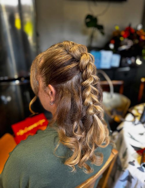 Back view of a woman with medium-length hair styled in a half-up bubble braid, featuring softly puffed sections down the center with loose curls left flowing.
