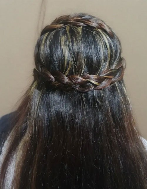 Back view of a woman with long dark hair styled in a half-up crown braid wrapped across the back of the head, with the remaining hair left straight and loose.