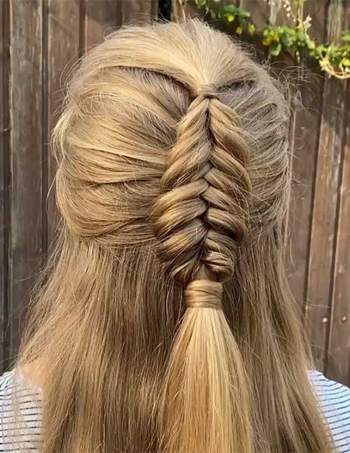 Back view of a woman with blonde hair styled in a half-up Dutch braid, featuring a raised central braid secured at the back with loose hair flowing below.