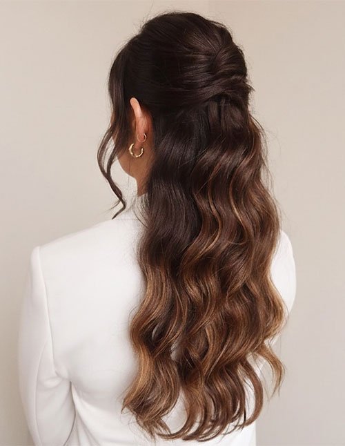 Back view of a half-up half-down hairstyle with softly lifted crown volume and long, loose waves, featuring dark brown hair with warm balayage ends.