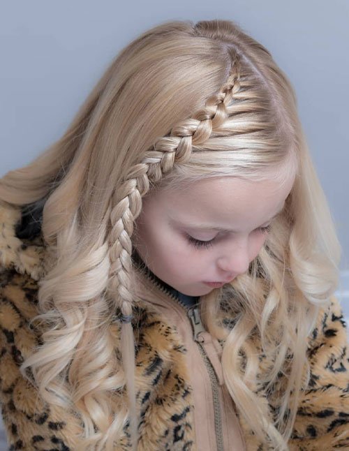 Young girl with blonde curled hair styled with a half-up lace braid along one side, with the braid ending in a small three-strand plait.