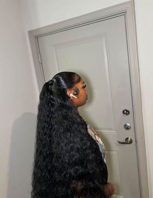 Side view of a woman with a sleek half-up ponytail, wearing long wavy hair down her back with styled baby hairs.