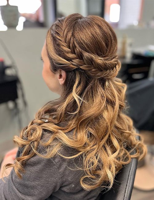 Side view of a woman with medium-length brown hair styled in a half-up side braid, with soft loose curls cascading over the shoulders.