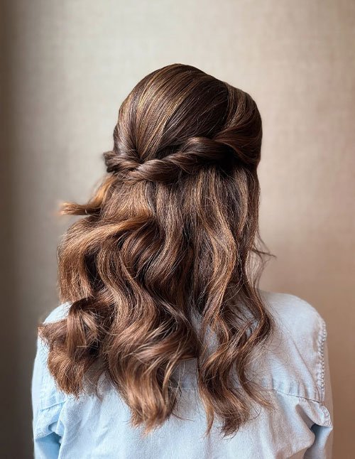 Back view of medium-length brown hair styled in loose waves with a half-up twist wrap pinned across the back of the head.