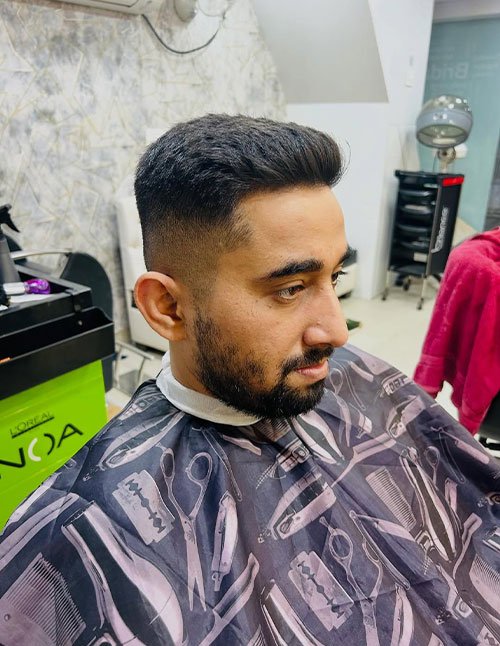 Side-angle view of a man with a high fade haircut for a square face, featuring short faded sides and a longer top brushed back with a neat beard.