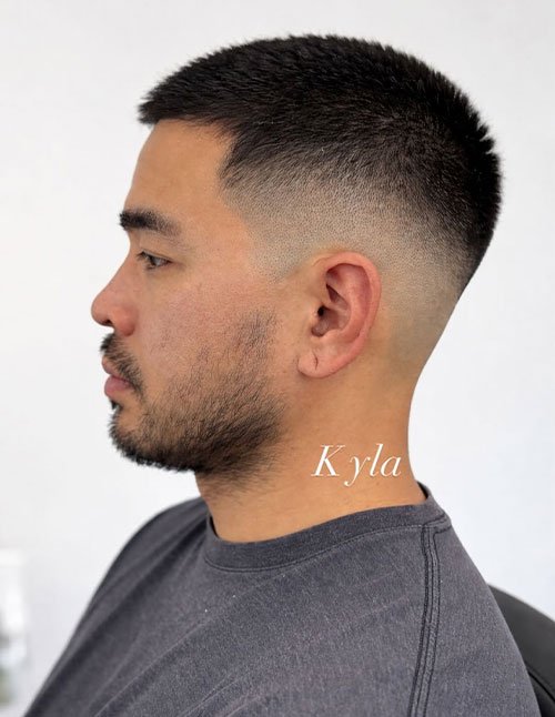 Side profile of a man with a high skin fade and very short textured hair on top, blending from bare skin up into a dark, cropped cut.