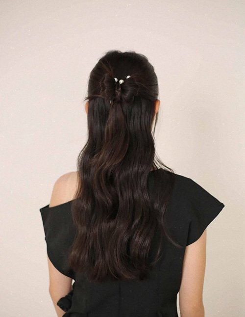 Holiday half-up twist on long wavy hair with a small pearl clip, back view.