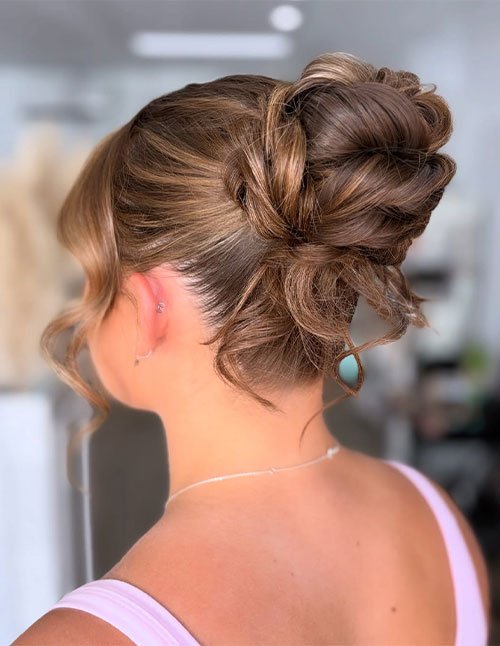 Knotted bun updo with a sleek base and loose curled tendrils, side view.