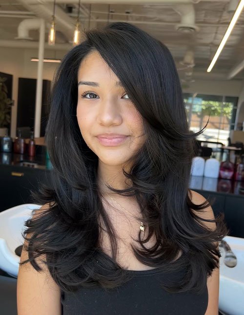 Woman with a layered medium-length haircut styled with a soft side part and smooth, voluminous layers.