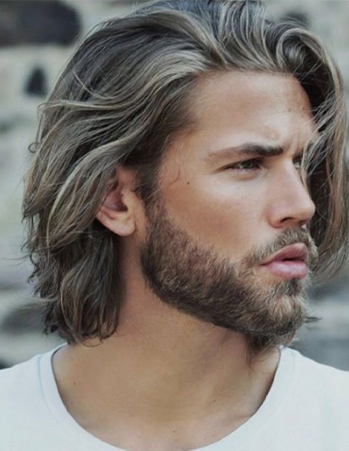 Side-profile of a man with a medium-length layered haircut, textured waves, and long face-framing pieces swept back.