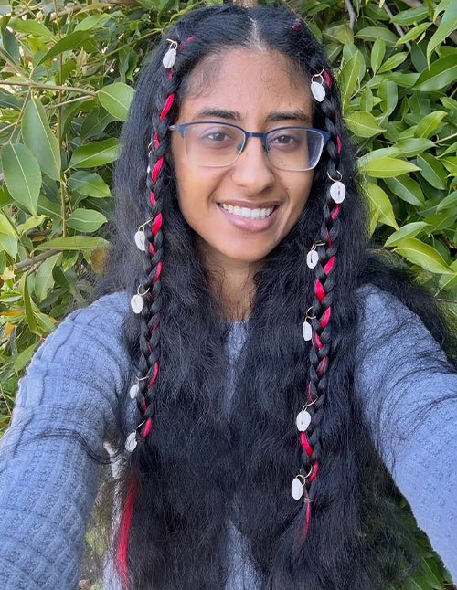 Two long accent braids wrapped with bright ribbon, finished with small shell-like charms, set against loose wavy hair.