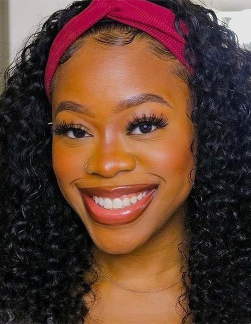 Girl with long, tight curly hair wearing a wide red headband, with curls framing the face and styled edges.
