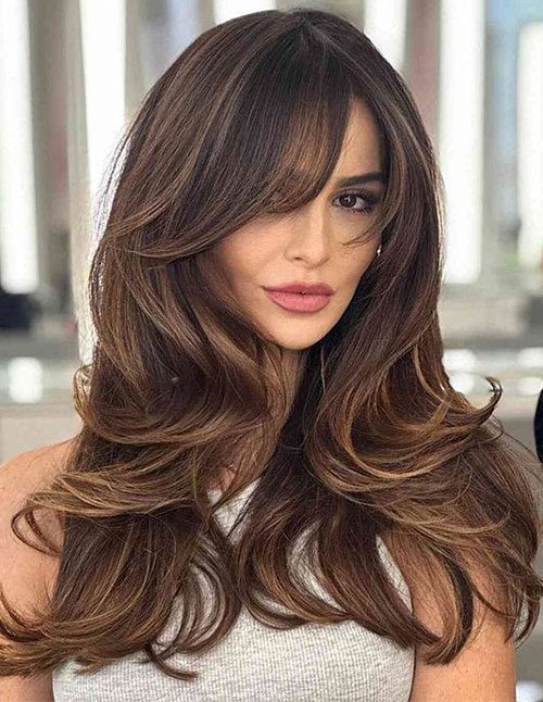 Woman with long, voluminous layers and side-swept long bangs.
