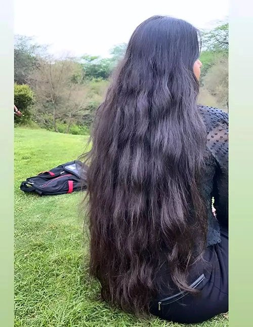 Long natural dark hair with soft waves flowing down the back while sitting on grass outdoors.