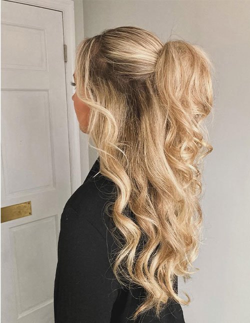 Loose half-up hairstyle with soft blonde waves and a lifted ponytail.