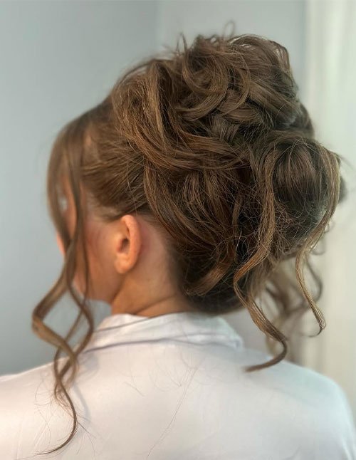 Side-back view of a woman wearing a loose updo with softly twisted hair gathered at the back and a few curled strands left out around the neck.