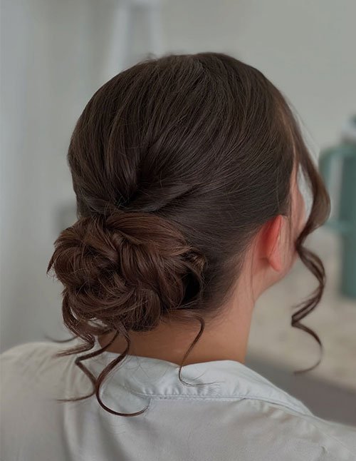 Back view of a sleek low bun at the nape with soft, curled face-framing strands left out on both sides.