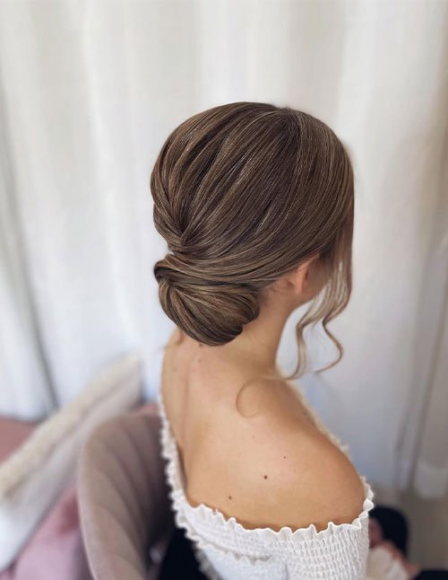 Sleek low bun hairstyle with smooth, side-swept sections gathered into a neat chignon at the nape, with a soft face-framing curl.