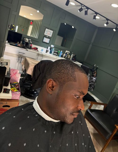 Side view of a man with a low Caesar crop, featuring very short textured hair and a sharp clean line-up around the forehead and temple area.