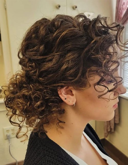 Side profile of a woman with curly hair styled into a low curly bun, with loose ringlets and soft volume at the crown.
