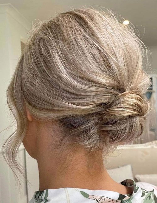 Back view of blonde hair swept into a loose low messy bun at the nape, with soft volume and a face-framing strand left out.
