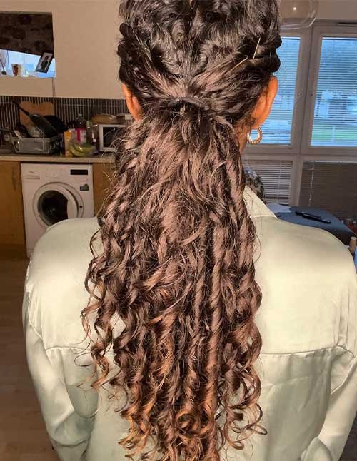 Back view of a woman with naturally curly hair styled in a low ponytail, featuring soft twists at the crown and defined curls flowing down the back.
