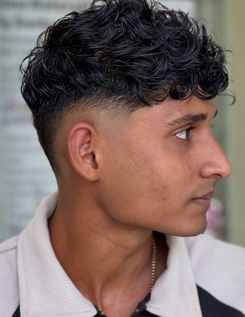 Side profile of a man with natural curly hair on top and a low taper fade, featuring a soft blend around the temples and ear.