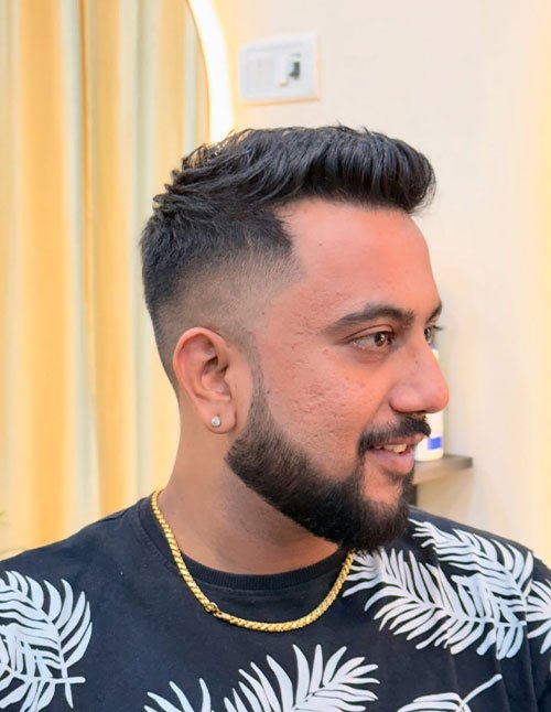 Side profile of a man with a low taper fade haircut, short textured top, and a neatly groomed full beard.