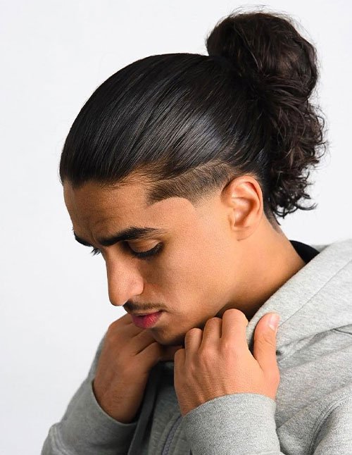 Man with man bun undercut hairstyle featuring tied-back long hair and shaved sides.