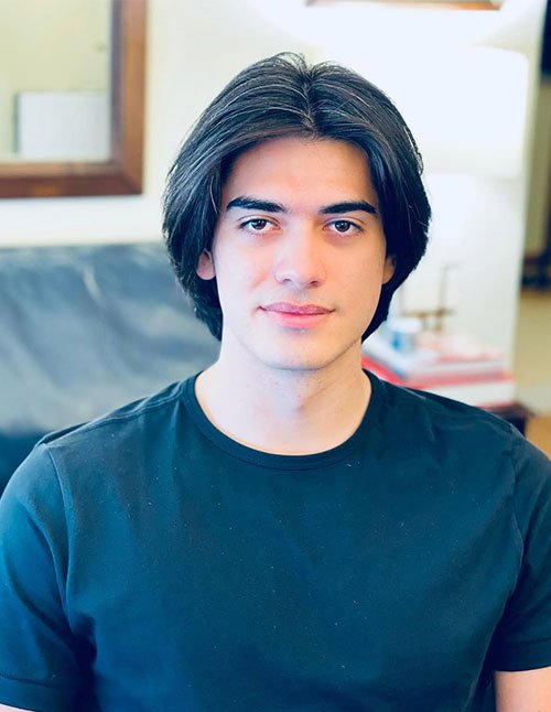 Masculine medium-length haircut with soft layered bangs parted at the center, framing the face naturally.