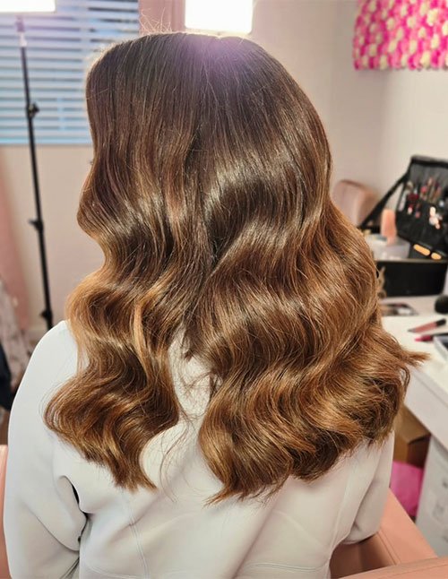 Back view of medium hair styled in soft, glossy waves with a warm brown tone.