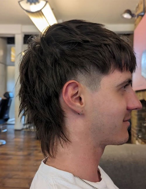 Side-profile of a man with a medium-length textured cut and a clean low taper on the sides, with longer layers in the back.