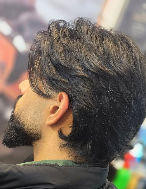 Side view of a man with a medium-length flow haircut, soft layers, and natural volume sweeping back over the ears.