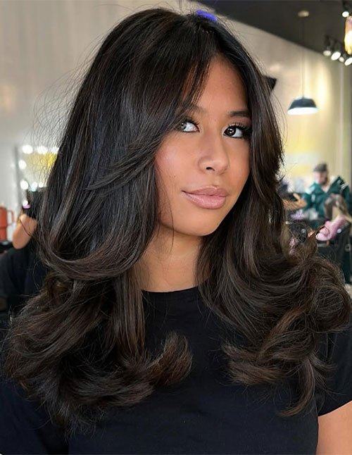 One woman with medium-length dark hair styled in layered, voluminous waves with feathered ends, photographed indoors.