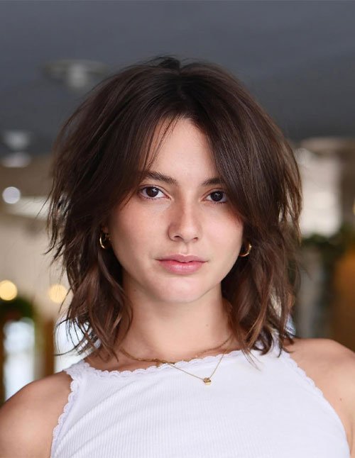 One woman with a medium-length haircut featuring short, choppy layers and a soft center part, photographed indoors.