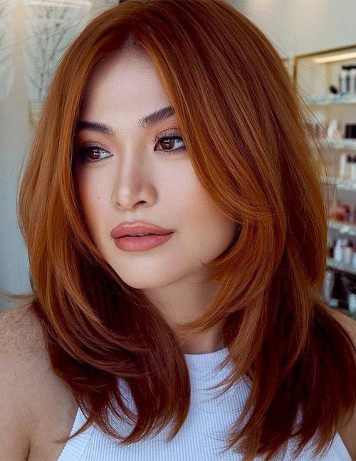 One woman with medium-length straight hair and long layers, styled with a soft center part in a warm copper color.