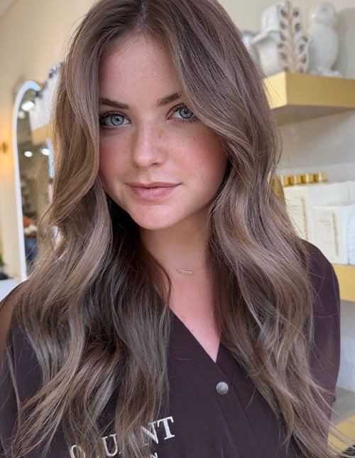 One woman with medium-length hair styled in soft layers and loose, natural waves, photographed indoors in a salon.