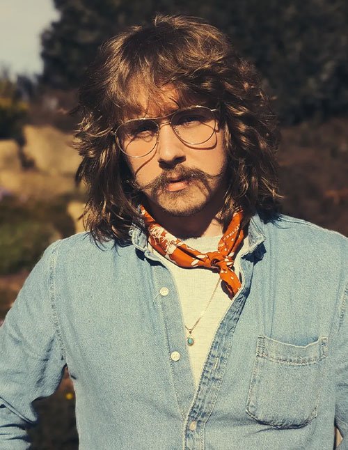 Man with long layered hair and full bangs, wearing glasses and a bandana, with thick texture around the sides and back.