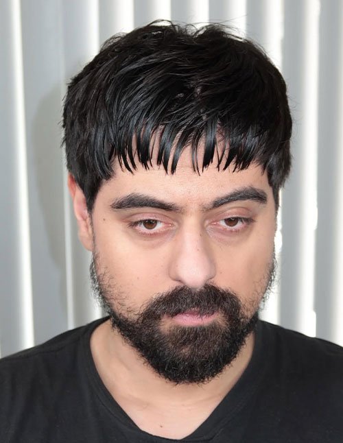 Man with a messy Caesar haircut featuring a short, uneven fringe and natural texture, paired with a full beard.