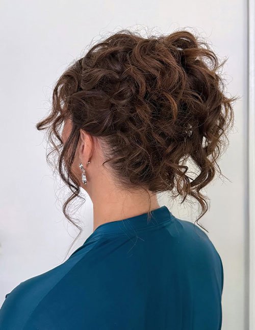 Messy curly updo with loose textured curls pinned at the back, soft tendrils framing the neck.