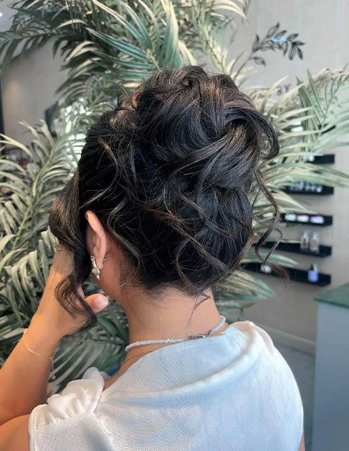 Back view of a girl with curly hair styled in a messy bun, with loose curls softly framing the neck and sides.