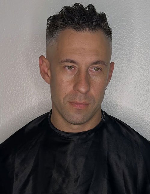 Front view of a man with a modern skin fade haircut and a short, textured top styled upward, with clean faded sides.