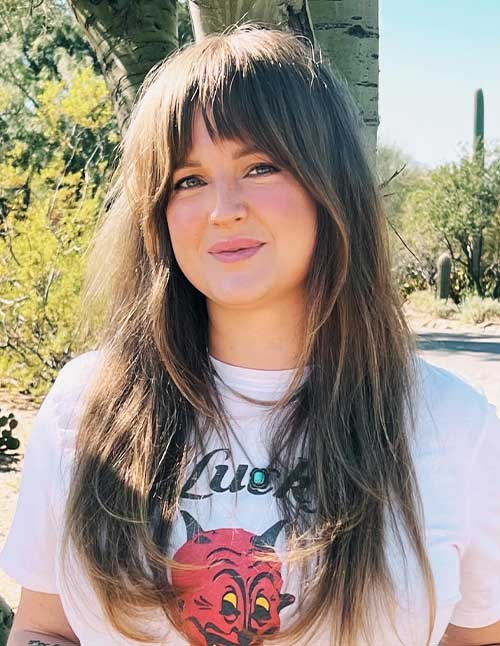 Woman with long layered hair and natural face-framing bangs outdoors.