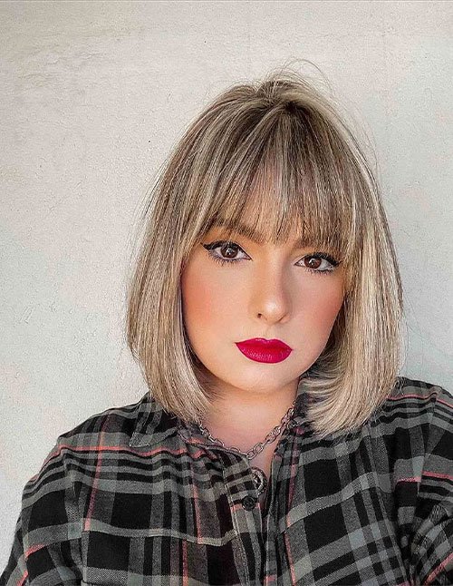 Neck-length bob haircut with straight bangs and soft blonde color.